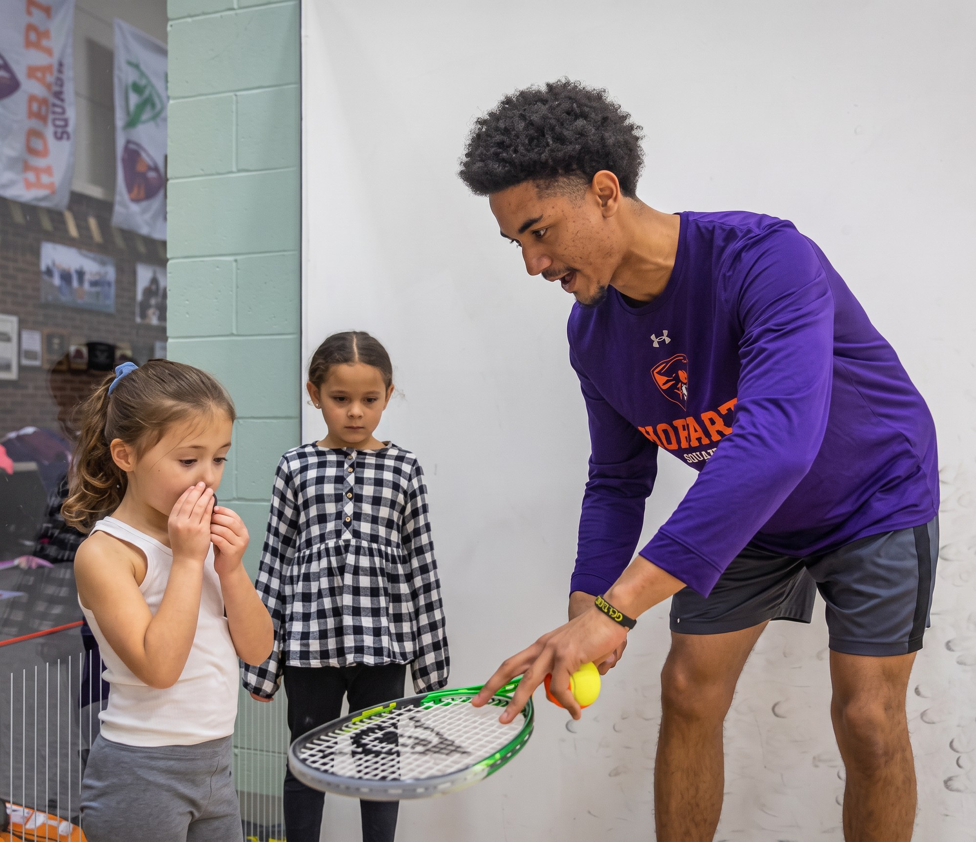 Coach Raji Davenport teaching a group of young children on a squash court