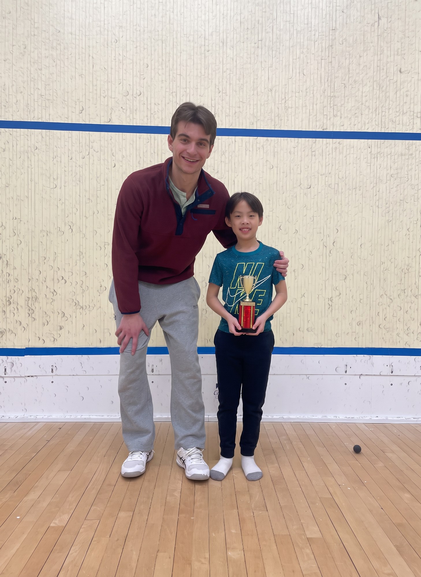 Coach posing on court with a junior player holding a trophy