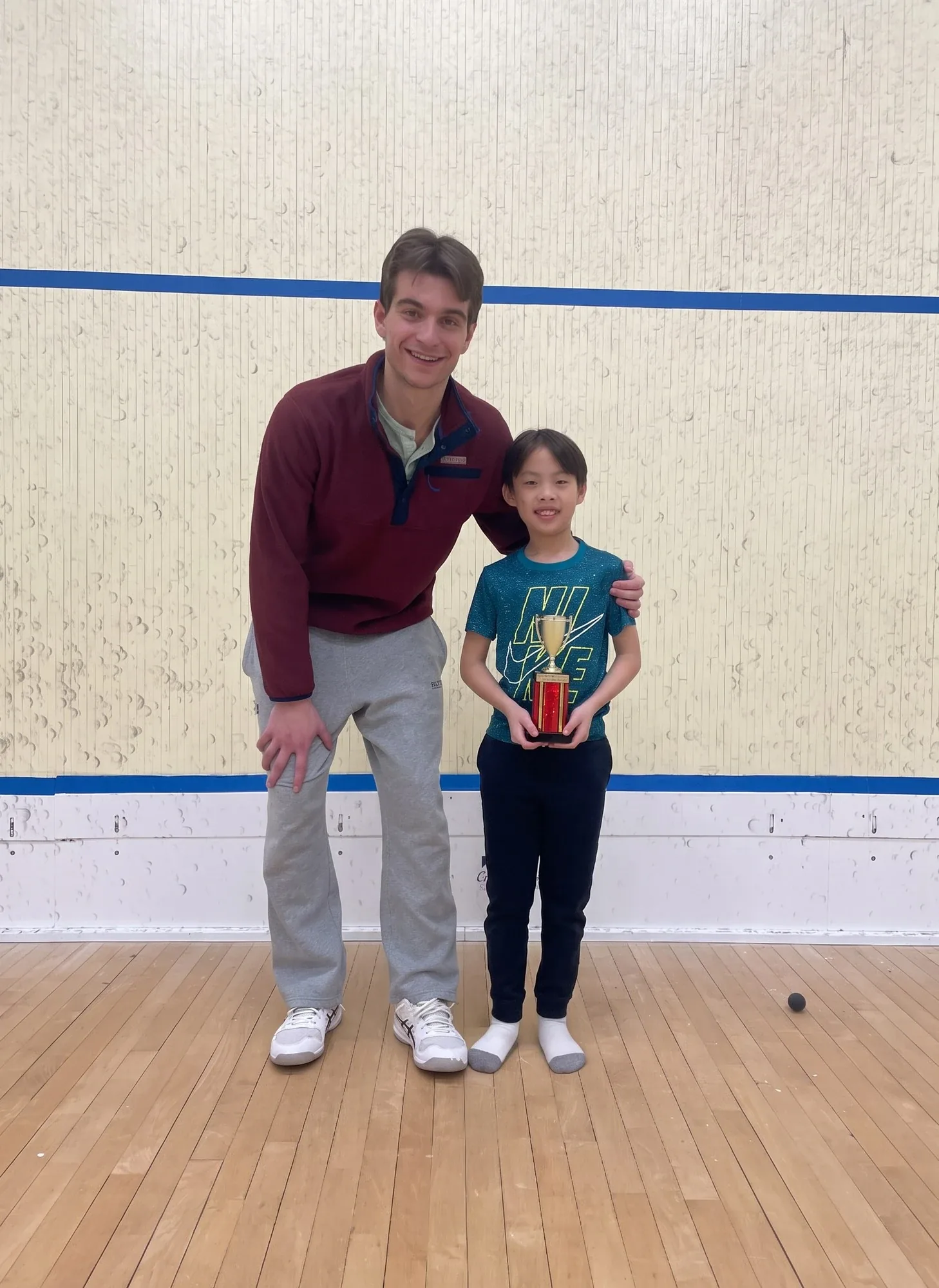 Coach posing on court with a junior player holding a trophy
